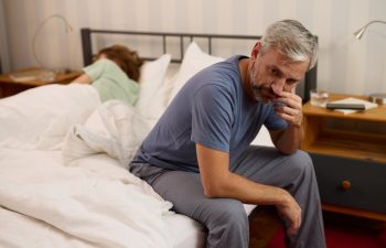 Mature man looking worried while his wife sleeps in the background