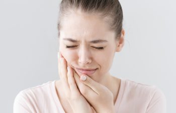 Closeup of beautiful teenage girl isolated on gray background touching her face and closing eyes with expression of horrible suffer from health problem and aching tooth showing dissatisfaction.